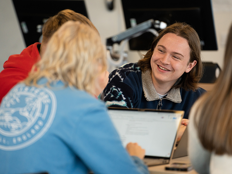 A group of smiling students sat round a table in a classroom